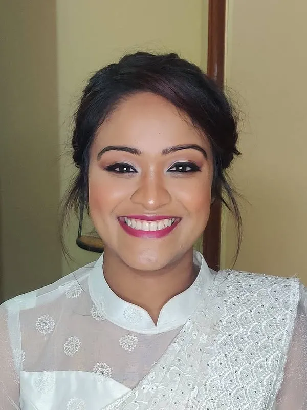 Smiling bride with braided updo, winged liner and berry lip in white saree