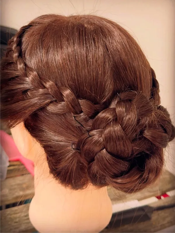 Back view of halo braid flowing into a braided flower bun on a mannequin head