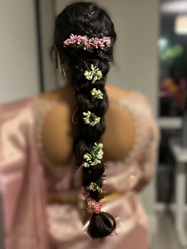 Back view of a long loose braid threaded with pink and white fresh flowers throughout