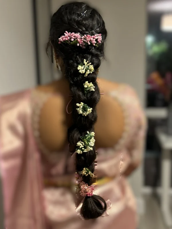 Back view of a long loose braid threaded with pink and white fresh flowers throughout